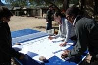 Students working on project plans atop a table tennis table outdoors.