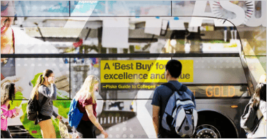 People are walking pass by a bus which has commercials on it