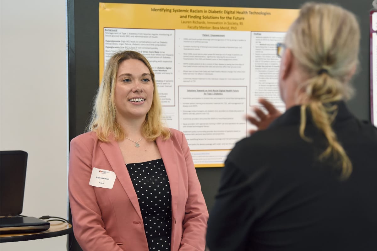 Two people are discussing a poster in front of the poster on the wall