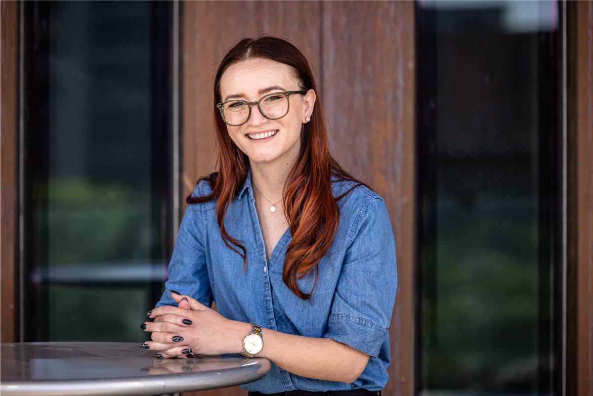 A person wearing glasses is smiling at the camera while sitting on the table